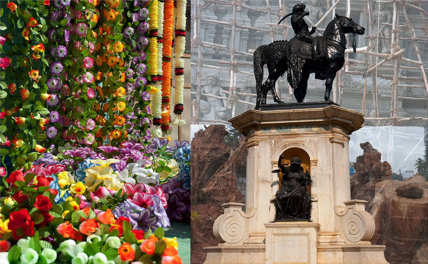 Several orange, purple, pink and red plastic flowers. To the right of it is a man seated on a horse. In the background is a temple under construction and chopped trees.