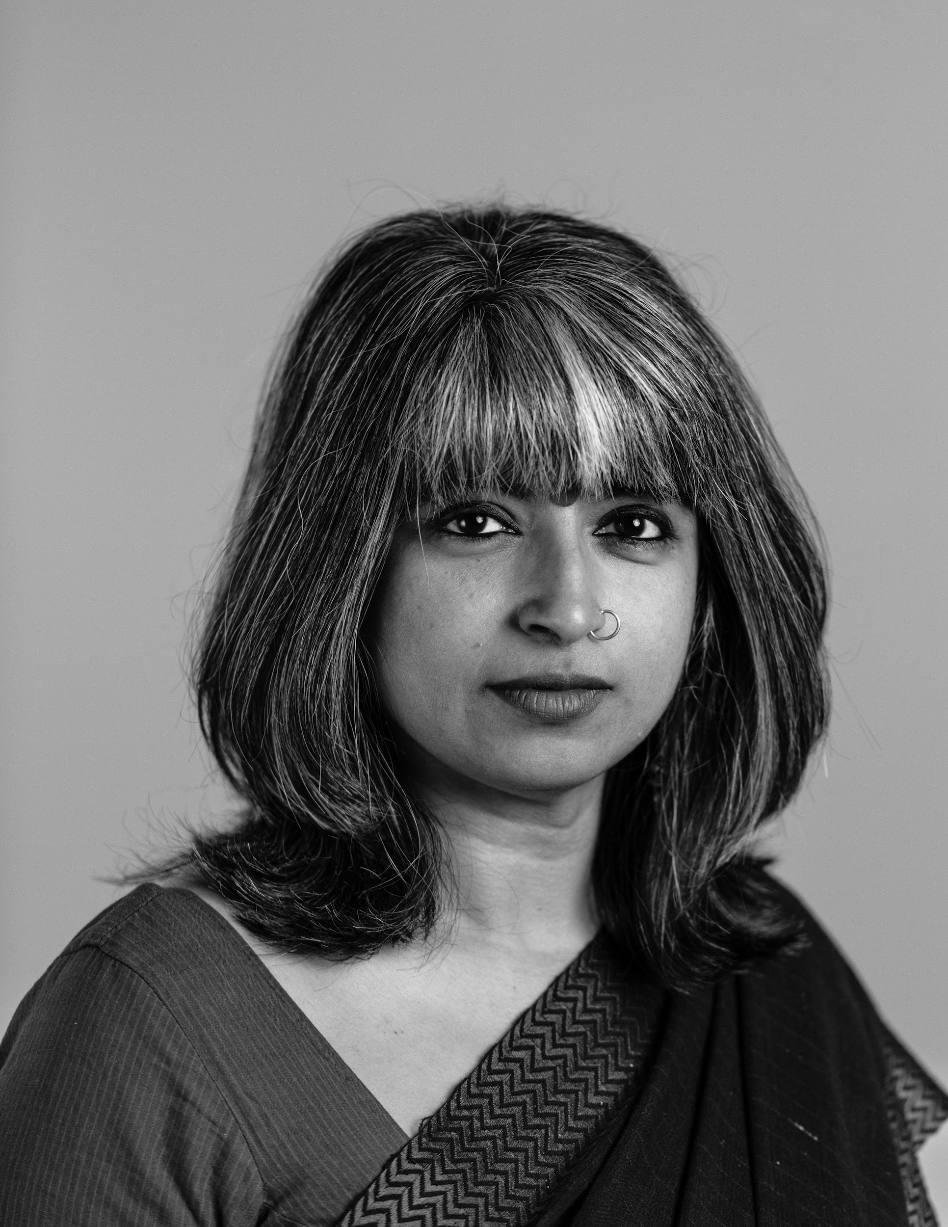 A woman in black and white at a slight angle looking into the distance. She has hair until her shoulders with bangs the front sections are light.