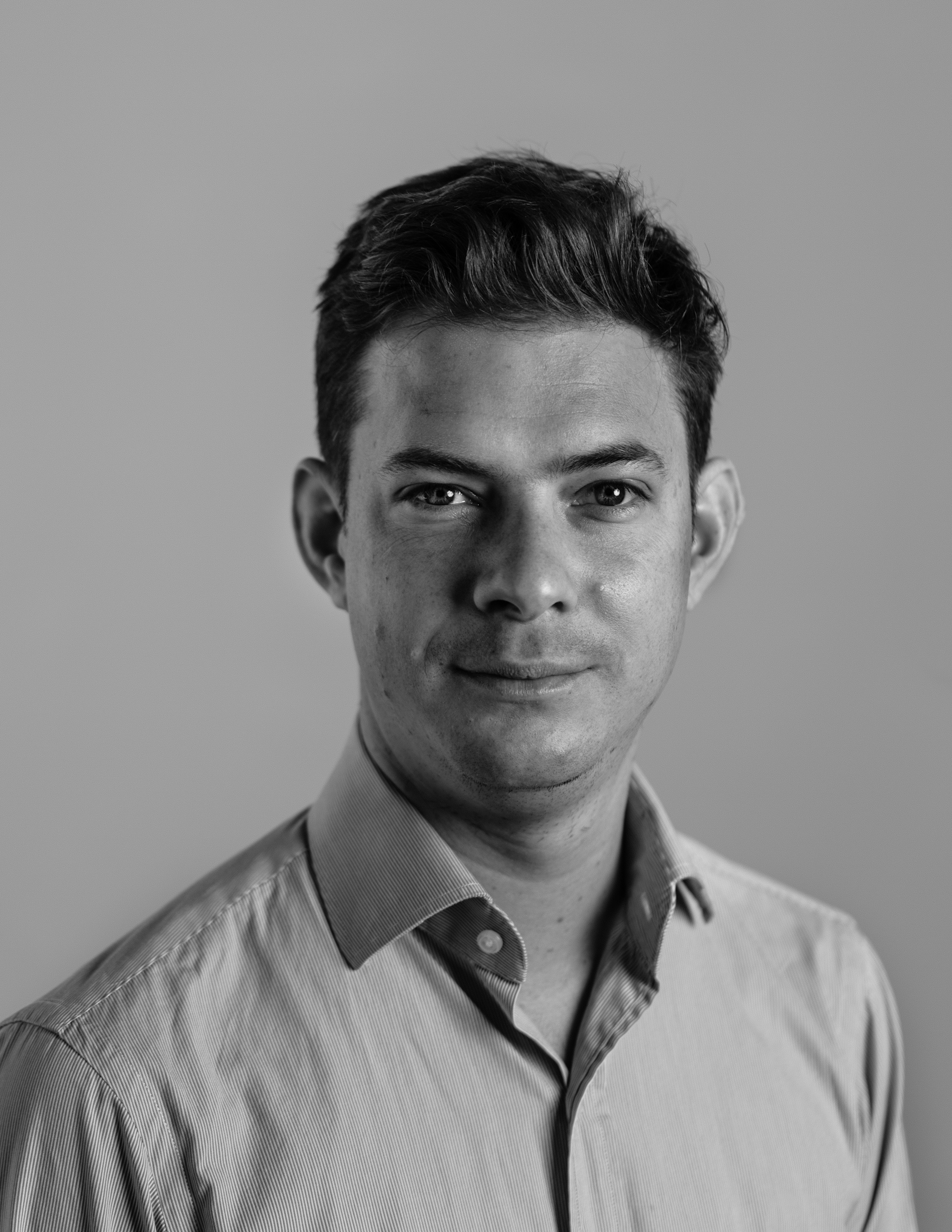 Nathaniel Gaskell in black and white wearing a collared shirt and looking directly into the camera smiling slightly.