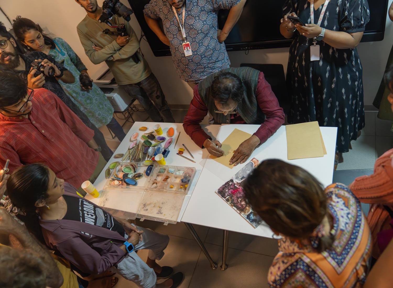 A person painting something surrounded by group of people.